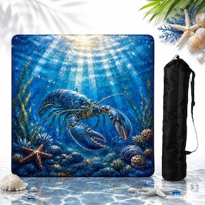 May include: A square-shaped beach towel featuring a vibrant underwater scene with a large blue lobster, a starfish, and coral reefs under sunlit water, accompanied by a black cylindrical carrying bag with a shoulder strap for easy transport.