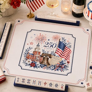 May include: A rectangular mahjong mat featuring a patriotic design with Independence Hall, the Liberty Bell, a document labeled We The People, and an American flag. The center graphic displays 250 YEARS with fireworks, surrounded by blue and red floral accents on a white background. Four dark blue tile racks are positioned around the mat, with white mahjong tiles displaying various symbols and characters.