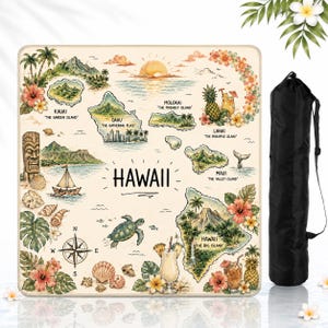 K&ouml;nnte beinhalten: Eine quadratische Matte mit einer detaillierten Karte von Hawaii, verziert mit Illustrationen von Inseln, einer Tiki-Figur, einer Meeresschildkr&ouml;te, tropischen Blumen, Ananas und Cocktails. Der Text enth&auml;lt Inselnamen. Eine schwarze Tasche liegt bei.