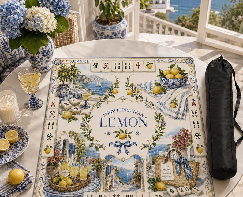 May include: A Mediterranean Lemon themed Mahjong game set with a decorative mat featuring lemons, coastal scenes, and the text "Mediterranean Lemon." Includes a black carrying case, a blue and white patterned plate, and a vase of blue hydrangeas.