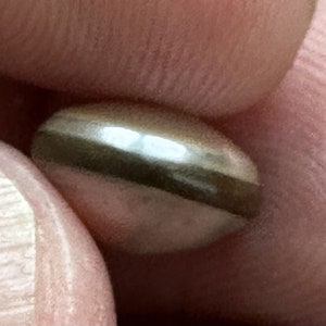 May include: A close-up of a silver-colored pill with a dark gray band around the middle.