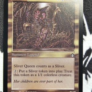 May include: A Magic: The Gathering card featuring the "Sliver Queen." The card has a brown and gold border with an illustration of a creature. Text includes "Summon Legend" and game instructions. The card is marked 7/7.