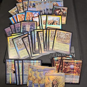 May include: A collection of various Magic: The Gathering trading cards arranged in a fan pattern. The cards feature diverse illustrations, including landscapes, artifacts, and characters, with some displaying holographic foil finishes and text.
