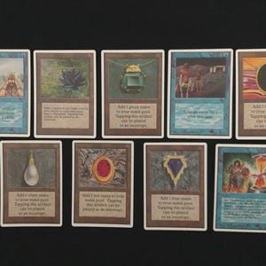 Könnte beinhalten: Eine Sammlung von neun Magic: The Gathering Sammelkarten, die in zwei Reihen angeordnet sind. Die Karten zeigen verschiedene Illustrationen, darunter einen König, einen schwarzen Lotus, Edelsteine und eine Sanduhr, mit Text zu Spielregeln.