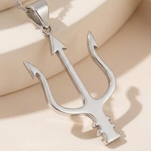 May include: A silver-colored pendant necklace featuring a trident design. The necklace has a delicate chain and a polished finish. The trident has three prongs and a central arrow-shaped point. The jewelry is displayed on a neutral background.