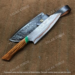 May include: A fixed-blade knife with a patterned steel blade featuring a distinct wavy line, a wooden handle with a bright green accent, and a black leather sheath embossed with a textured pattern and secured by a metallic snap button.