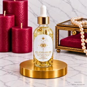 May include: A clear glass dropper bottle containing golden oil with botanical inclusions. The white label features gold text reading ALL EYES ON ME, GLAMOUR MAGIC RITUAL OIL, SHINE, RADIATE, BE SEEN, CARIS & CO. RITUAL APOTHECARY, and 2 oz.