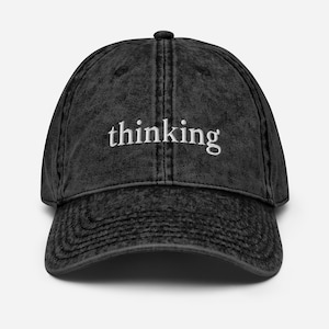 May include: A black, vintage-style baseball cap with the word "thinking" embroidered in white across the front. The cap has a curved brim and a distressed appearance, suggesting a worn-in look.