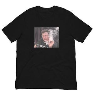 Op de afbeelding: Een zwart t-shirt met korte mouwen en een rechthoekige grafische print op de borst. De print toont een persoon met een koptelefoon op, die een brandende sigaar vasthoudt en een grote rookwolk uitblaast. De persoon draagt een zwart shirt met tekst.