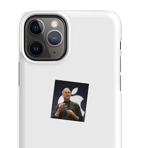 May include: A white smartphone case featuring a square sticker of Steve Jobs holding an early iPhone model in front of a large Apple logo. The case has a triple-lens camera cutout in the upper left corner and a smooth, matte-finish surface.