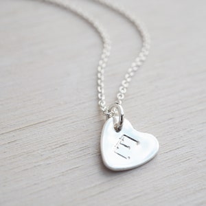 May include: A silver necklace with a heart-shaped pendant. The pendant has the letters "LL" engraved on it.