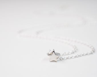 May include: A silver-toned necklace featuring a small, five-pointed star pendant. The star charm is accented with a single, clear, round-cut gemstone set into one of its points. The pendant is attached to a delicate, thin silver-toned chain.