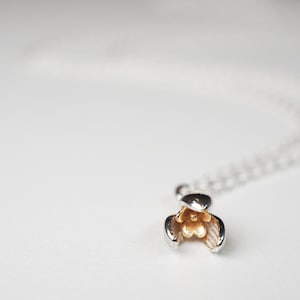 May include: A silver chain necklace with a delicate flower pendant. The flower is made of silver and gold, with the center of the flower being gold.