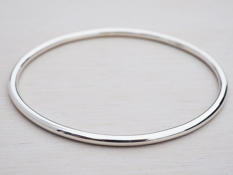 May include: A simple silver bangle bracelet with a smooth, rounded finish.