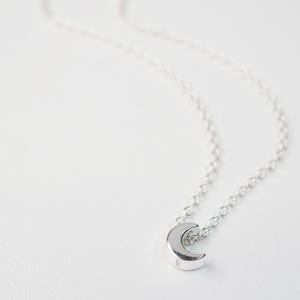 May include: A silver crescent moon pendant necklace on a delicate silver chain.
