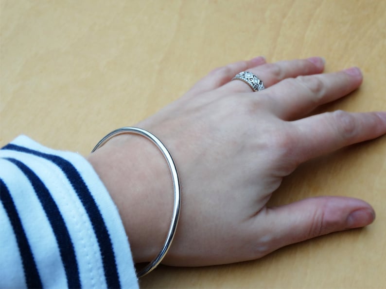 May include: A silver bangle bracelet on a person's wrist. The bracelet is simple and has a smooth, polished finish.