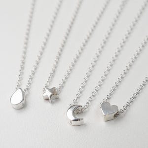May include: Four silver necklaces with different charms: a teardrop, a star, a crescent moon, and a heart.