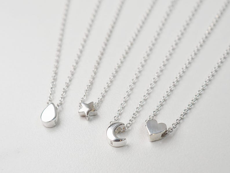 May include: Four silver necklaces with different charms: a teardrop, a star, a crescent moon, and a heart.
