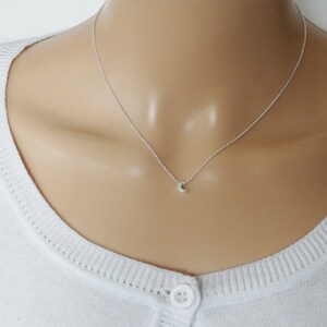May include: A delicate silver necklace with a small crescent moon pendant.