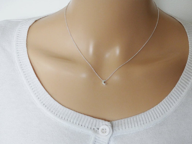 May include: A delicate silver necklace with a small crescent moon pendant.