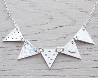 May include: A silver necklace with five triangle pendants. The pendants are textured with different patterns, including dots, hammered metal, and a small heart.