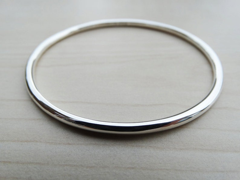 May include: A simple silver bangle bracelet with a smooth, rounded surface.