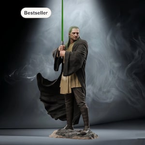Puede incluir: Figura detallada de un personaje de una franquicia de ciencia ficción, sosteniendo un sable de luz verde. La figura viste una túnica oscura y una túnica beige, de pie sobre una base rocosa. La palabra "Bestseller" está en un óvalo blanco en la esquina superior izquierda.