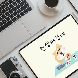 May include: A laptop, tablet, and camera are arranged on a white surface. The tablet displays a cartoon Shiba Inu sleeping at a desk. A coffee cup, phone, mouse, and headphones are also visible.