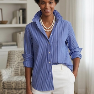 May include: A blue and white vertical striped button-down shirt with a ruffled collar and long sleeves, paired with white trousers and a double-strand pearl necklace. The shirt features a front button placket and folded cuffs at the wrists.