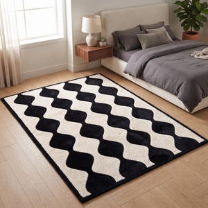 May include: A rectangular area rug featuring a repeating black and cream-colored wavy, scalloped pattern. The design consists of vertical, undulating stripes that create a series of interconnected, rounded shapes across the entire surface.