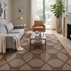May include: A living room with a grey sofa, a brown leather armchair, and a wooden coffee table with a glass top. A large rug with a geometric pattern in shades of brown covers the floor. A potted plant and a fireplace complete the room's decor.