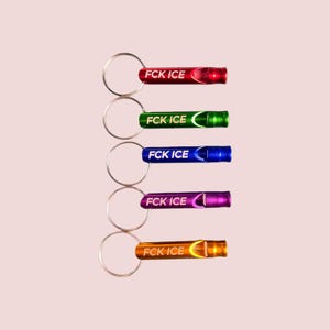 May include: A collection of five metal whistles in red, green, blue, purple, and orange, each attached to a silver keyring. The text "FCK ICE" is printed on each whistle. The whistles are arranged vertically against a light pink background.