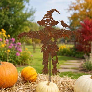 May include: A rust-colored metal garden stake featuring a cutout silhouette of a scarecrow wearing a wide-brimmed hat with a jack-o'-lantern face. A small bird is perched on the scarecrow's left shoulder, and the figure has frayed edges.