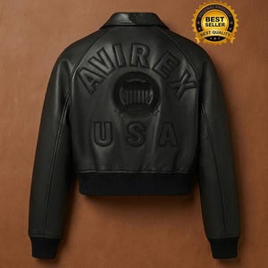 Op de afbeelding: Zwarte leren bomberjack met het woord "AVIREX" en "USA" in reli&euml;f op de rug. De jas heeft een geribbelde zoom en manchetten en een kleine kraag. Een gouden "Best Seller" sticker staat in de rechterbovenhoek.