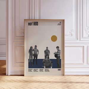 May include: A framed movie poster for "Hot Rod" with a beige and navy blue background. The poster features a group of people and a gold circle. The title "HOT ROD" is at the top. The year "2007" is in the bottom right corner.