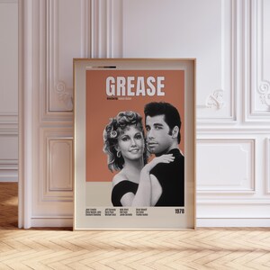 Può includere: Poster cinematografico incorniciato del film "Grease" con John Travolta e Olivia Newton-John. Il poster ha uno sfondo color pesca con il titolo del film in grandi lettere bianche. L'anno 1978 è nell'angolo in basso a destra.