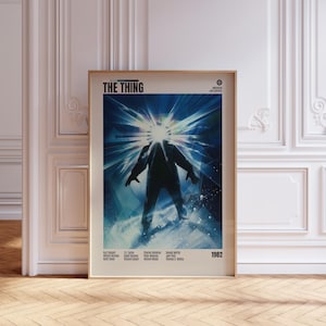 May include: Framed movie poster for "The Thing" with a blue and white graphic of a silhouetted figure with a bright light emanating from its head. The title "THE THING" is at the top, with the year "1982" at the bottom.