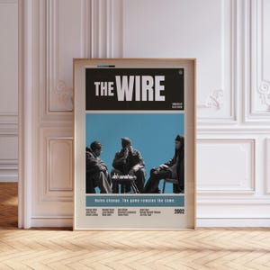Pode incluir: Pôster emoldurado da série de TV "The Wire". O pôster apresenta o título do programa em letras brancas em bloco sobre um fundo azul com três figuras jogando xadrez. O texto "Rules change. The game remains the same." está abaixo.
