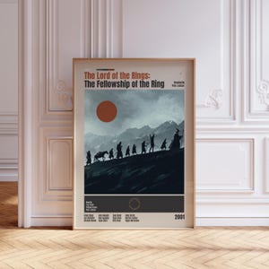 May include: A vertical poster titled The Lord of the Rings: The Fellowship of the Ring. It features a dark silhouette of a group walking across a mountain ridge under a large orange sun against a cloudy sky. The text includes credits and the year 2001.