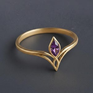 Peut inclure: Une bague en or avec une pierre précieuse violette de taille marquise sertie dans un motif de feuille stylisé. La bague a un anneau délicat et une forme unique et élégante. La pierre est d'un violet vif, sertie dans un sertissage en or.