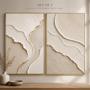 May include: A set of two rectangular wall art pieces featuring textured cream and beige abstract layers with gold-painted edges, framed in thin gold metal. The text SET OF 2 LUXURY TEXTURED WALL ART is printed above the two vertical canvases.