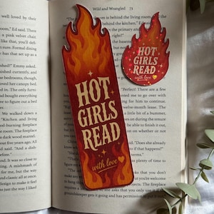May include: A tall rectangular bookmark and a smaller circular sticker, both featuring a flame design in shades of orange, red, and yellow. The text HOT GIRLS READ with love is printed in a bold, light-colored font on both items.