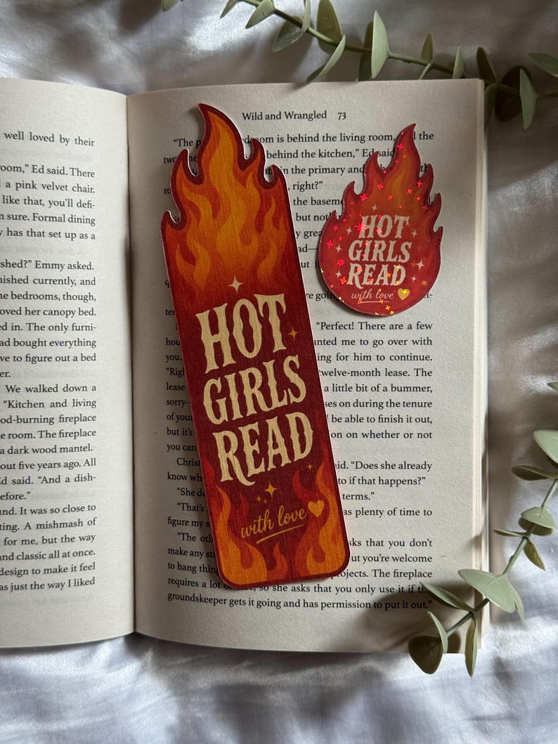May include: A tall rectangular bookmark and a smaller circular sticker, both featuring a flame design in shades of orange, red, and yellow. The text HOT GIRLS READ with love is printed in a bold, light-colored font on both items.