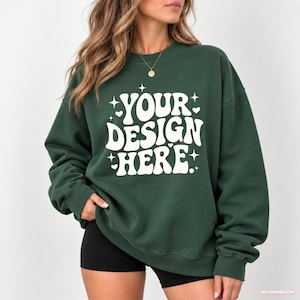 Könnte beinhalten: Ein dunkelwaldgrünes Sweatshirt mit Rundhalsausschnitt und weißem Text, der in einer fetten, wellenförmigen Schrift YOUR DESIGN HERE lautet. Das Design ist mit kleinen weißen Sternen und Herzen verziert, die um den Schriftzug verteilt sind.