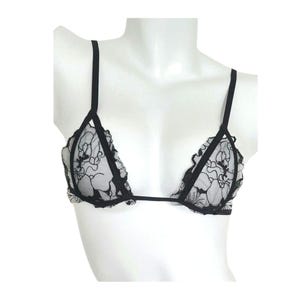 May include: A black and white bralette featuring a sheer white mesh base with an intricate black floral lace overlay. The garment has thin black adjustable shoulder straps, a triangular cup design, and a thin black band connecting the two cups.