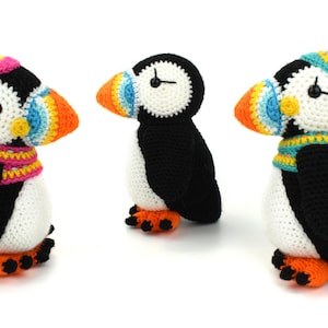 May include: Three crocheted stuffed puffins wearing colorful hats and scarves. The puffins are black and white with orange beaks and feet.