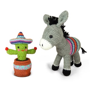 May include: A grey crocheted donkey with a colourful striped blanket and a black mane stands next to a green crocheted cactus wearing a colourful sombrero. The cactus is in a brown pot with blue and pink accents.