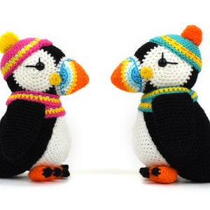 May include: Two crocheted puffins wearing colorful hats and scarves. The puffins are facing each other and have black and white bodies with orange beaks.