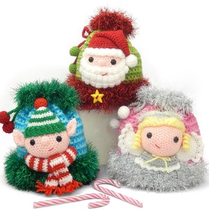 May include: Three crocheted Christmas stocking ornaments. The first is a red and green Santa Claus stocking with a white beard and a red pom-pom. The second is a blue and green elf stocking with a red and white striped scarf. The third is a pink and white angel stocking with blonde hair and a silver halo.