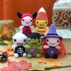 Op de afbeelding: Vijf gehaakte Halloween-figuren: een skelet, een heks, een Frankenstein, een duivel en een suikertje. De figuren zitten op een boek met herfstbladeren eromheen.